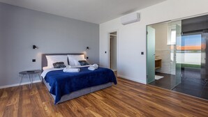 A modern bedroom with a bed, bedside tables, and a glass door leading to a balcony.