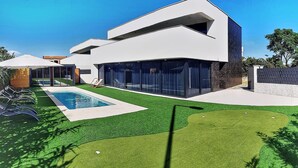 A modern two-story house with a swimming pool, a well-maintained lawn, and a patio area with lounge chairs.
