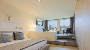 Una habitación de hotel moderna con una cama grande, un escritorio, una silla y un balcón con vistas a la ciudad.