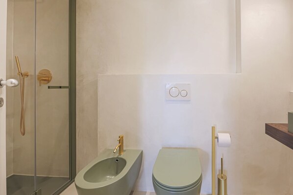 Un baño con bidé, inodoro y zona de ducha con mampara de vidrio.