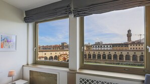 Habitación de hotel con un amplio ventanal con vistas a un paisaje urbano, un radiador y una mesita de noche con lámpara.