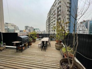 Enjoy al fresco dining on the rooftop terrace with a barbecue grill, table, and chairs, surrounded by lush greenery and city views.