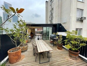 Enjoy al fresco dining on the rooftop terrace with a long dining table and comfortable seating, surrounded by lush greenery and a city view.