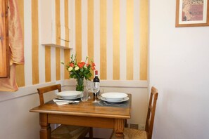 Una mesa de comedor preparada con platos, vasos y una botella, con una pared a rayas y un cuadro enmarcado al fondo.
