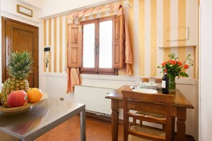 Eine Küche mit einem Holztisch, einer Obstschale, einem Fenster mit Vorhängen und einer Vase mit Blumen.