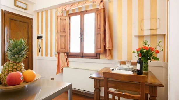 A kitchen with a wooden table, a fruit bowl, a window with curtains, and a vase with flowers. - Apartments Florence - Ariento Eva 1bdr San Lorenzo (Firenze)