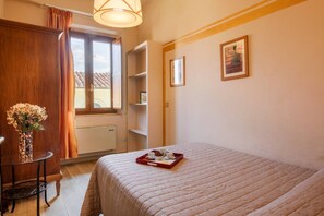 Une chambre à coucher avec un lit, une table de chevet ornée d’un vase, une fenêtre avec des rideaux et un plateau contenant des tasses et une pâtisserie.