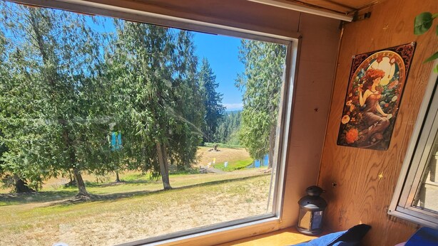 A cozy cabin interior with a large window overlooking a forest, a wooden ceiling, and a table with a tray and a notebook. - Boho Caravan themed, Vintage 1961 Oasis Camper (Monroe)