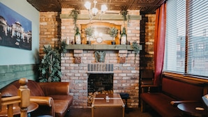 Une pièce chaleureuse avec une cheminée en briques, des canapés en cuir, une table en bois et une grande fenêtre avec des stores.