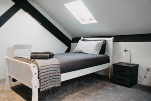 Un dormitorio con techo inclinado, una cama, una mesita de noche y un escritorio pequeño.