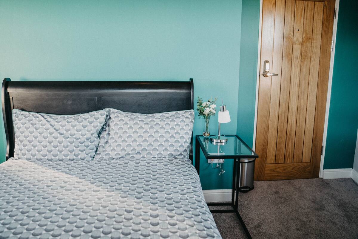 Ein Schlafzimmer mit einem Bett, einem Nachttisch, einer Lampe und einer Holztür.