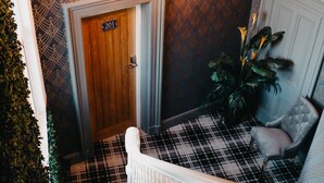Un escalier recouvert d’un tapis à carreaux, avec une rampe blanche et une porte portant l’inscription « 201 ».