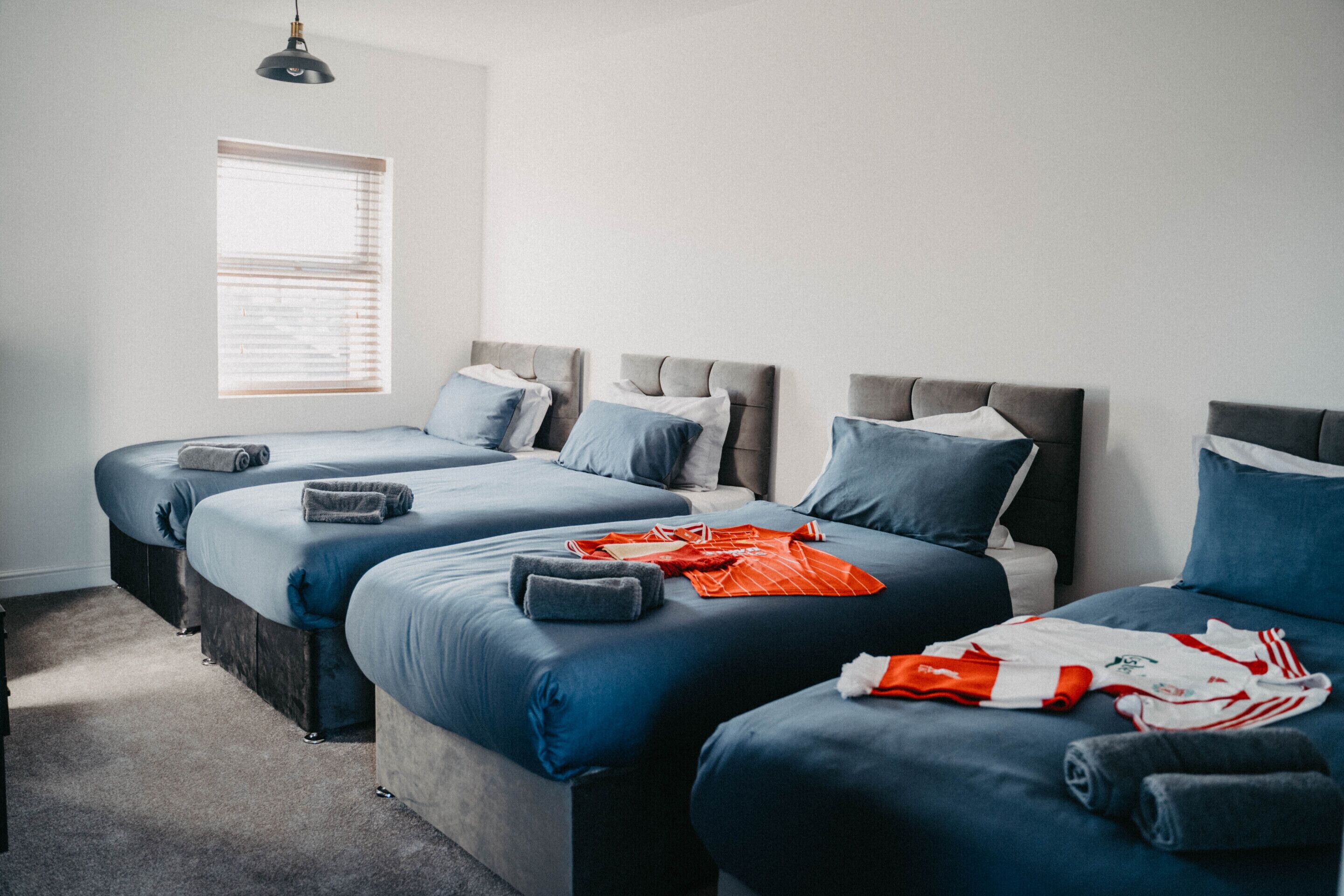 A hotel room with three beds arranged in a row, a window with blinds, and a hanging light fixture.