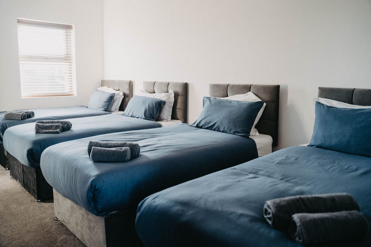 Ein Hotelzimmer mit drei nebeneinander stehenden Betten, jeweils mit blauer Bettwäsche und Kissen.