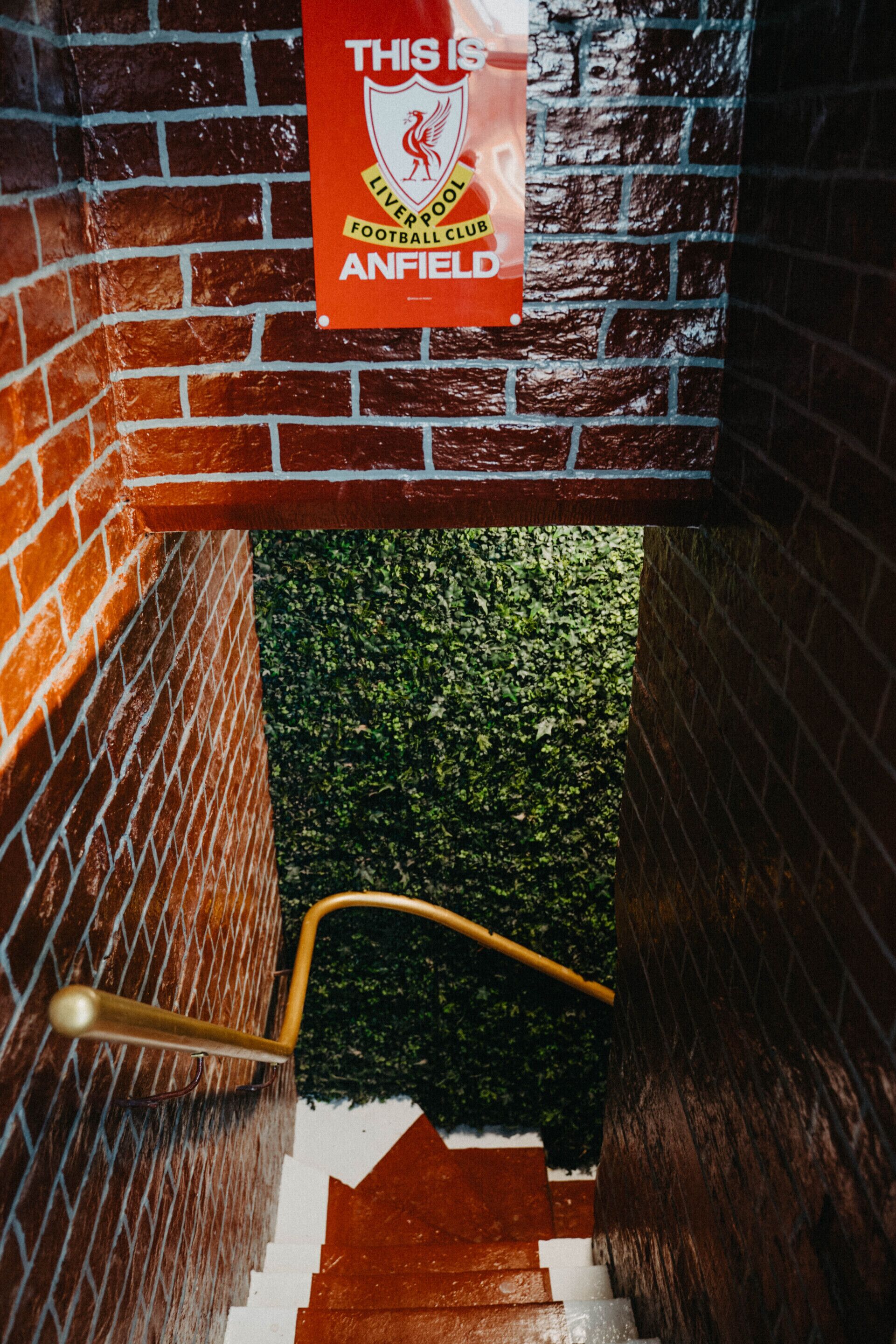 A staircase with a brick wall and a sign indicating the entrance to the Liverpool Football Club Anfield stadium.