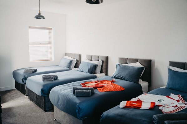 A bedroom with three beds arranged in a row, a window with blinds, and a hanging light fixture.