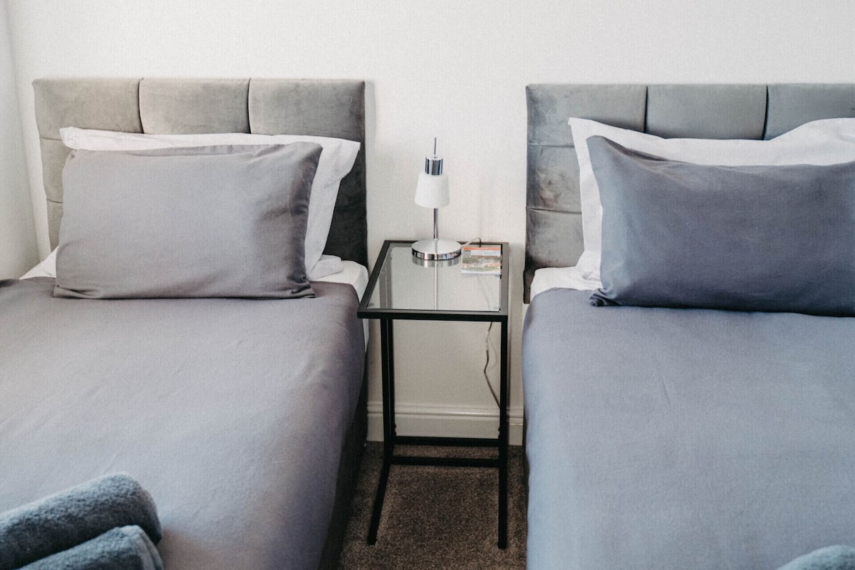 Ein Hotelzimmer mit zwei Einzelbetten, einem Nachttisch mit Lampe und einem kleinen Tisch.