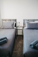 A hotel room with two single beds, a nightstand with a lamp, and a small table.