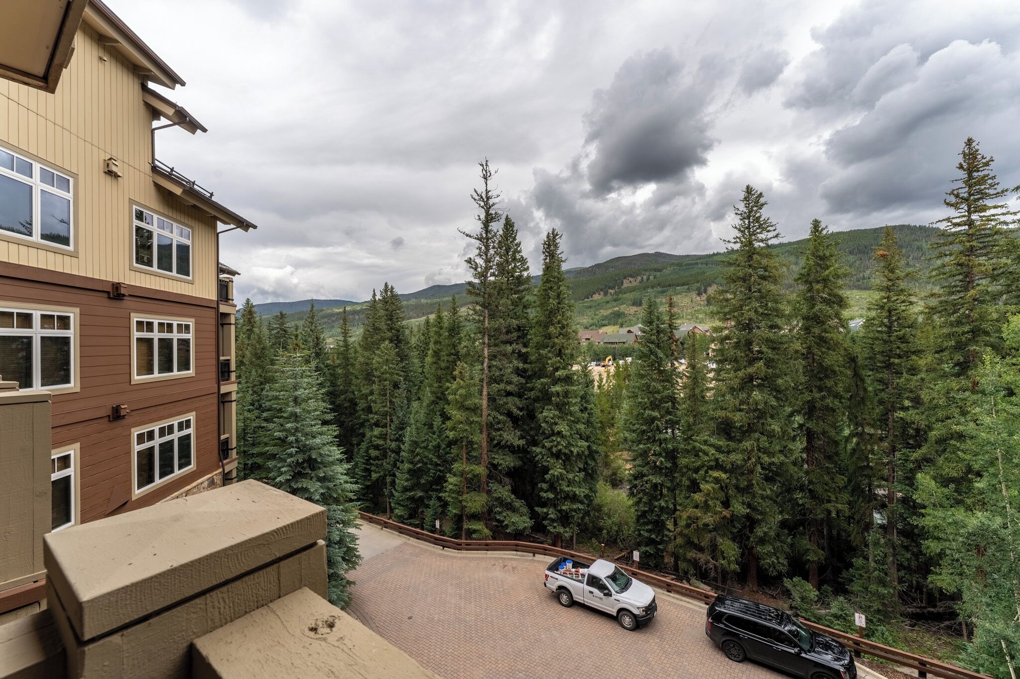 A multi-story building with a parking area and a view of a forested hillside.