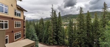A multi-story building with a parking area and a view of a forested hillside.