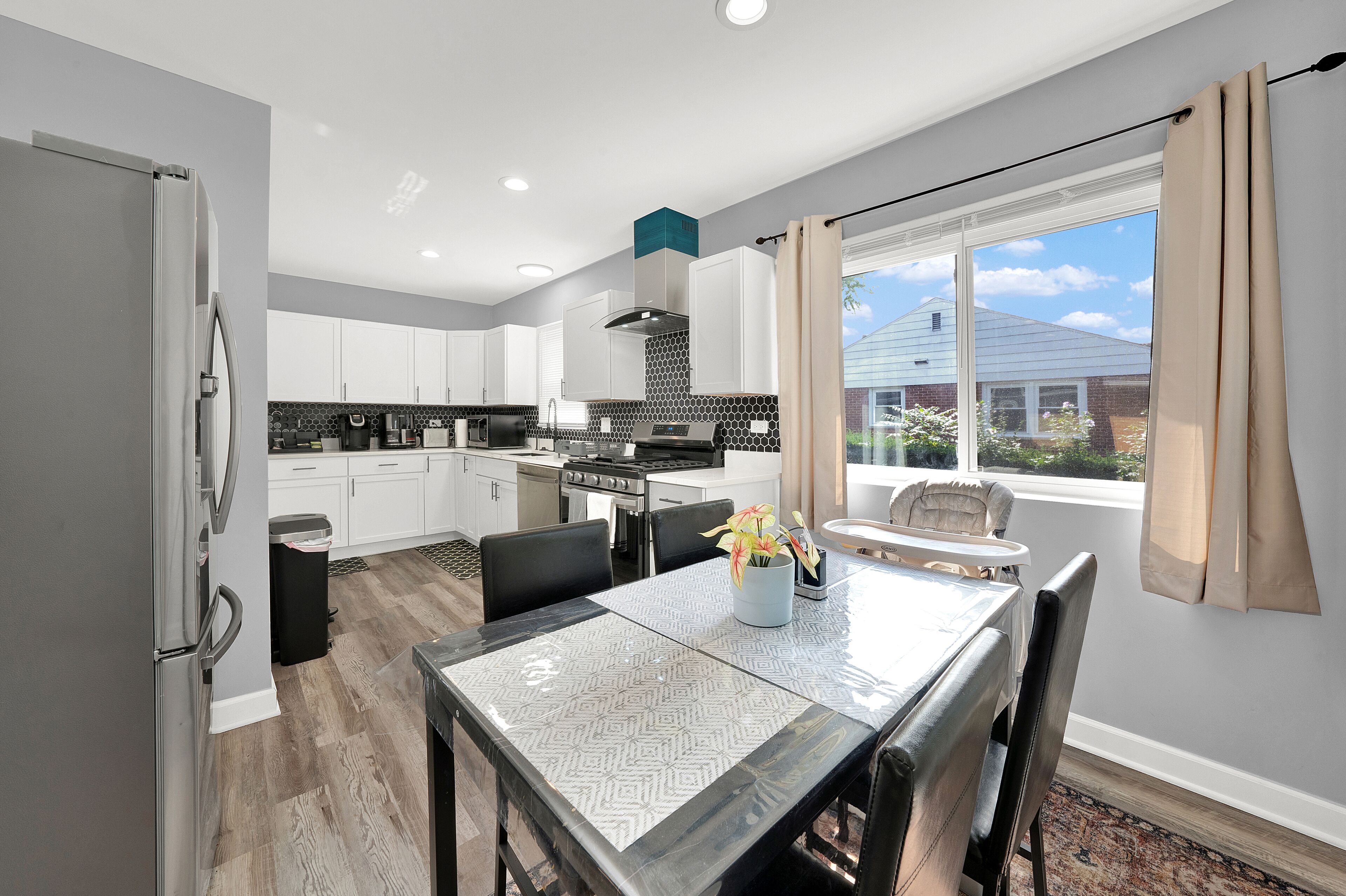 A modern kitchen with white cabinets, a stainless steel refrigerator, and a dining area with a table and chairs.