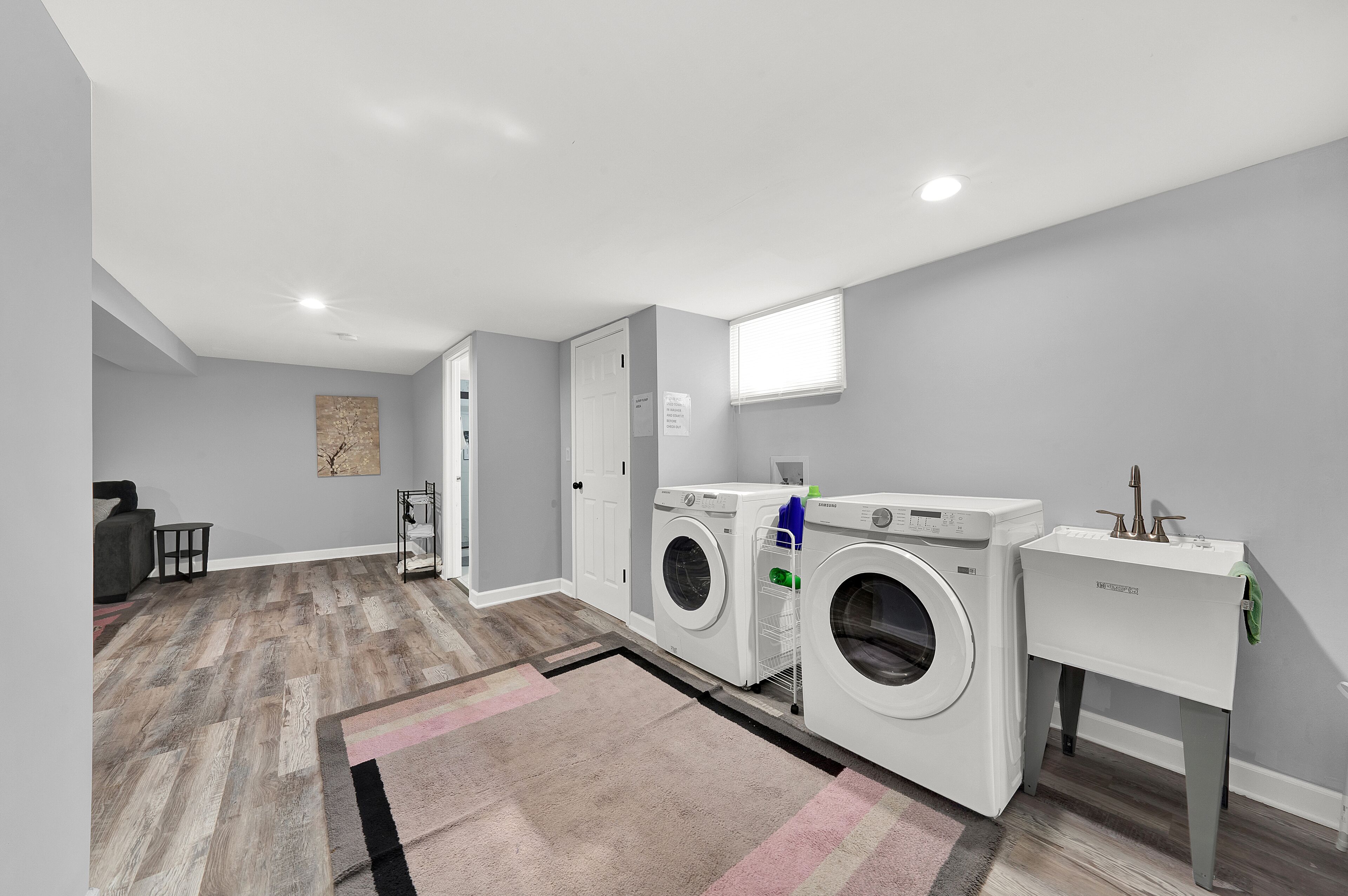A laundry room with two washing machines, a drying rack, and a sink.