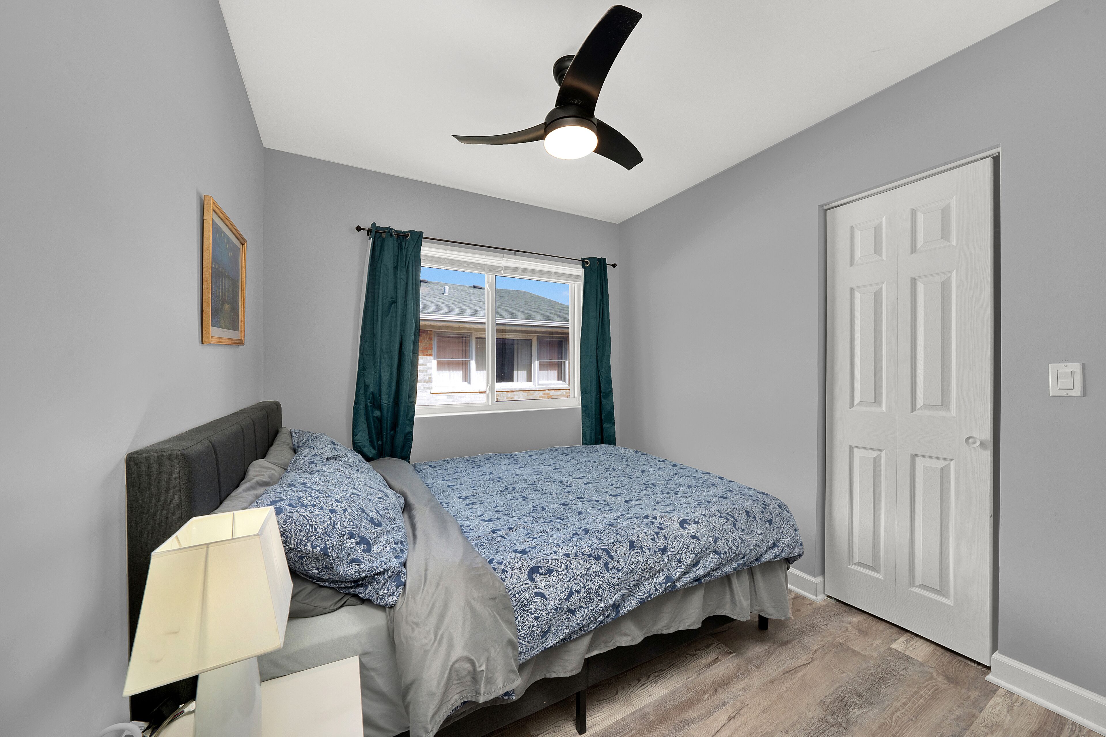 A bedroom with a bed, a ceiling fan, a window with curtains, and a door.