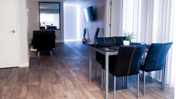 Una sala moderna con comedor, un televisor de pantalla plana montado en la pared y un ventanal con cortinas.