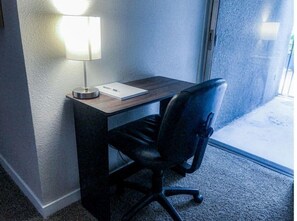 A small, dark-colored desk with a lamp, a chair, and a window.