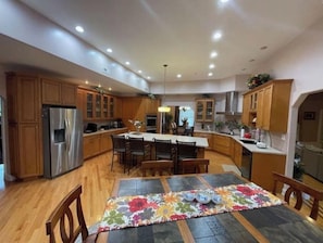 A spacious kitchen with wooden cabinets, a stainless steel refrigerator, a central island with chairs, and a dining table with a floral table runner. - Cozy Countryside  Getaway (Grovertown)