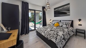 A modern bedroom with a large bed, a desk, and a view of a garden through a sliding door. - 3 bedroom awesome home in Labin (Labin)