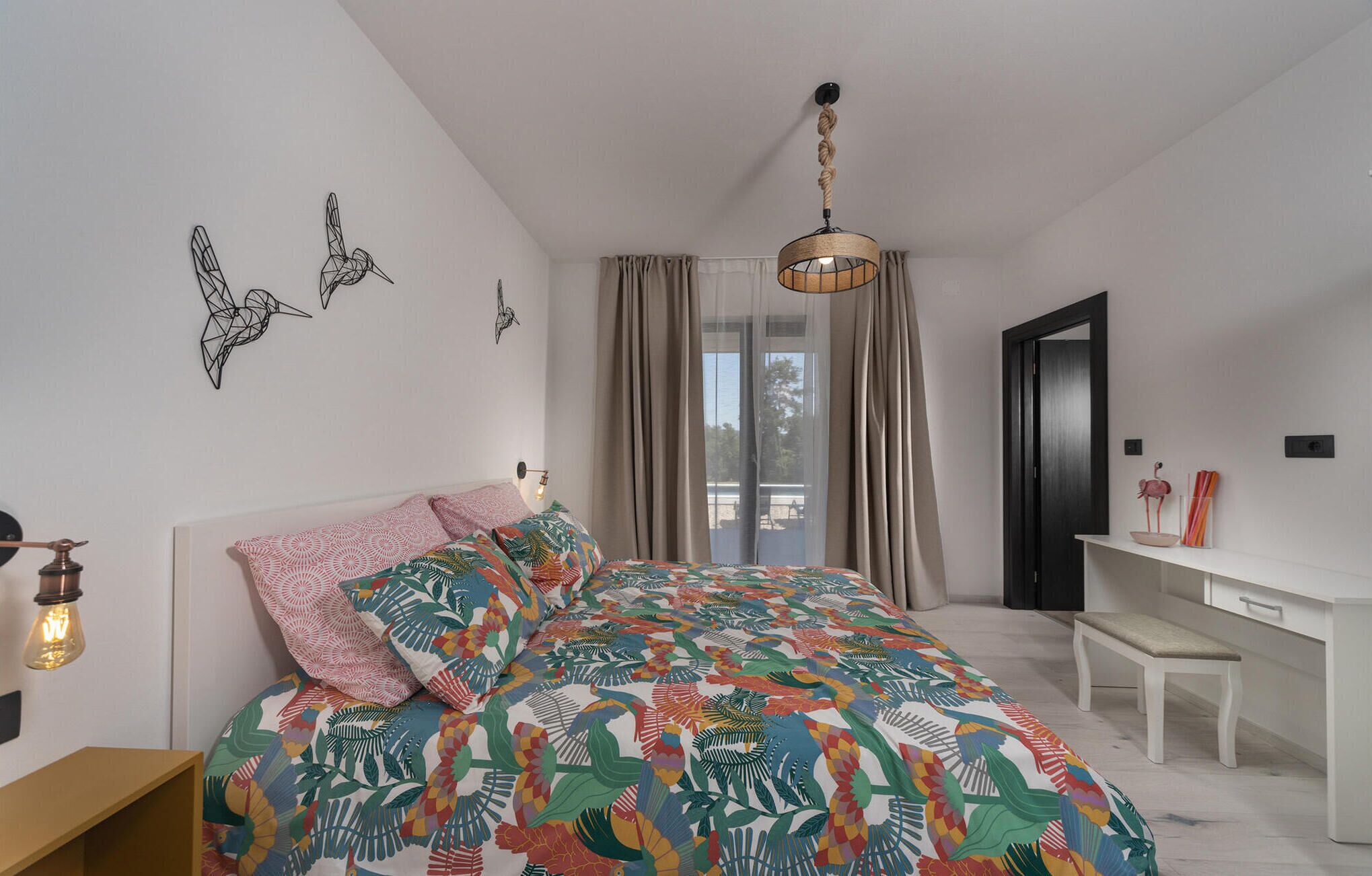 A bedroom with a bed, a desk, and a chair. There are curtains on the window, and a ceiling light fixture.