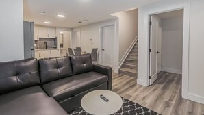 A modern living room with a black leather sofa, a round coffee table, and a kitchen in the background. - Kozy In Keswick (Suite) (Edmonton)