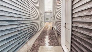A narrow pathway between two buildings with horizontal siding. - Kozy In Keswick (Suite) (Edmonton)
