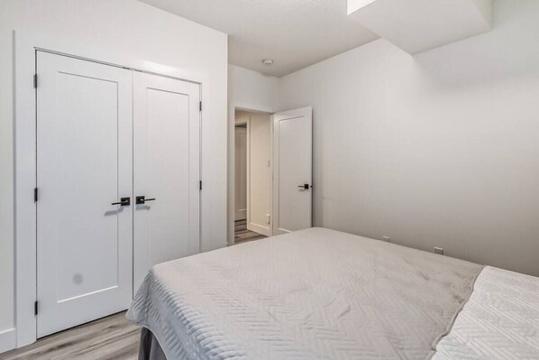A bedroom with a bed, two wardrobes, and a door leading to a hallway. - Kozy In Keswick (Suite) (Edmonton)