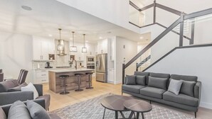 A modern living room with a grey sofa, a coffee table, and a kitchen area with a central island and bar stools. - Kozy In Keswick (Upper Suite) (Edmonton)