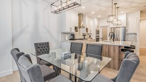 A modern kitchen with a central island, a dining area with a glass table, and a kitchen island with a built-in sink. - Kozy In Keswick (Upper Suite) (Edmonton)