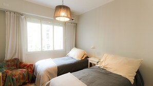 A bedroom with two beds, a window with curtains, a hanging lamp, and a small bedside table. - Amplio y Silencioso en Recoleta Luz (Buenos Aires)