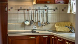 A kitchen with wooden cabinets, a hanging pot rack with various kitchen utensils, a wicker basket, and a modern faucet.