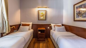 A hotel room with two single beds, a nightstand, a framed picture on the wall, and a window with curtains.