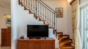 A staircase with wooden steps and black balusters, a flat-screen TV on a wooden cabinet, and a painting on the wall.