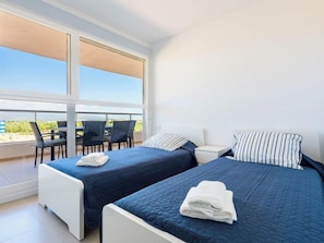 Habitación de hotel con dos camas, un balcón con sillas y vista al paisaje.