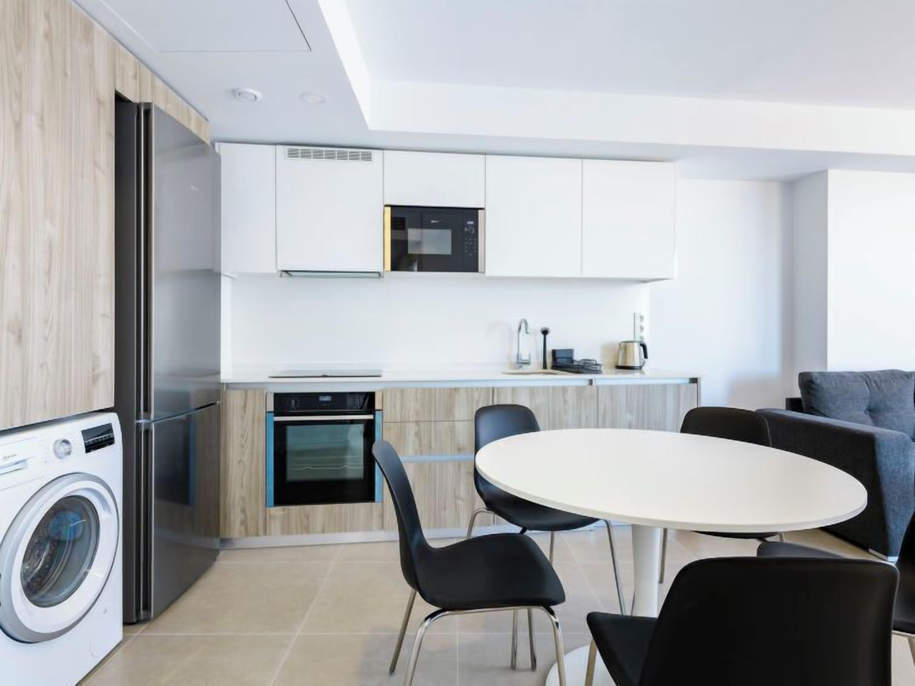 A modern kitchen with a built-in oven, a washing machine, and a dining area with a round table and chairs.