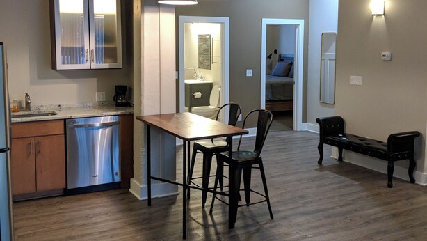 A modern kitchen with stainless steel appliances, a dining area with a wooden table and chairs, and a bench in the living area.