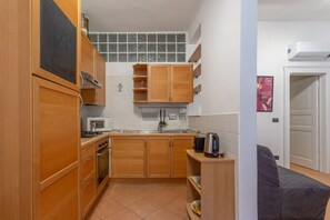 A compact kitchen with wooden cabinets, a microwave, a kettle, and a tiled backsplash.