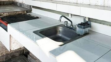 A kitchen with a stainless steel sink, a built-in grill, and a small trash bin.