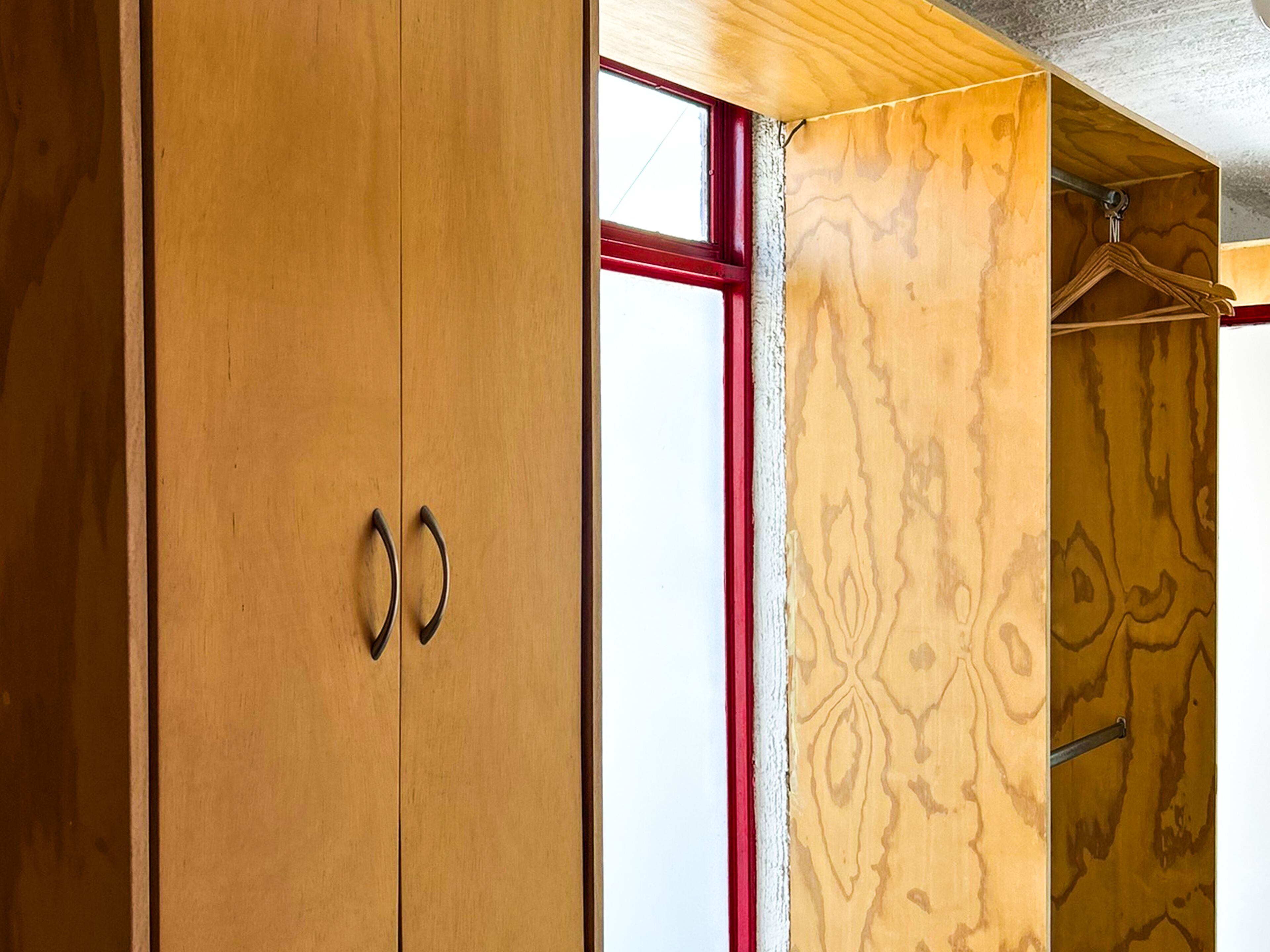 Une armoire en bois à deux portes, avec une fenêtre à cadre rouge.