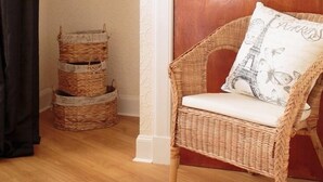 A wicker chair with a cushion, a wooden door, and stacked baskets against a wall. - The Corner House (Peebles)