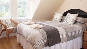 A bedroom with a bed, pillows, a chair, and a window. - The Corner House (Peebles)