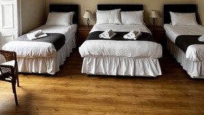 A hotel room with three single beds, a chandelier, a wooden floor, and a large window. - The Corner House (Peebles)